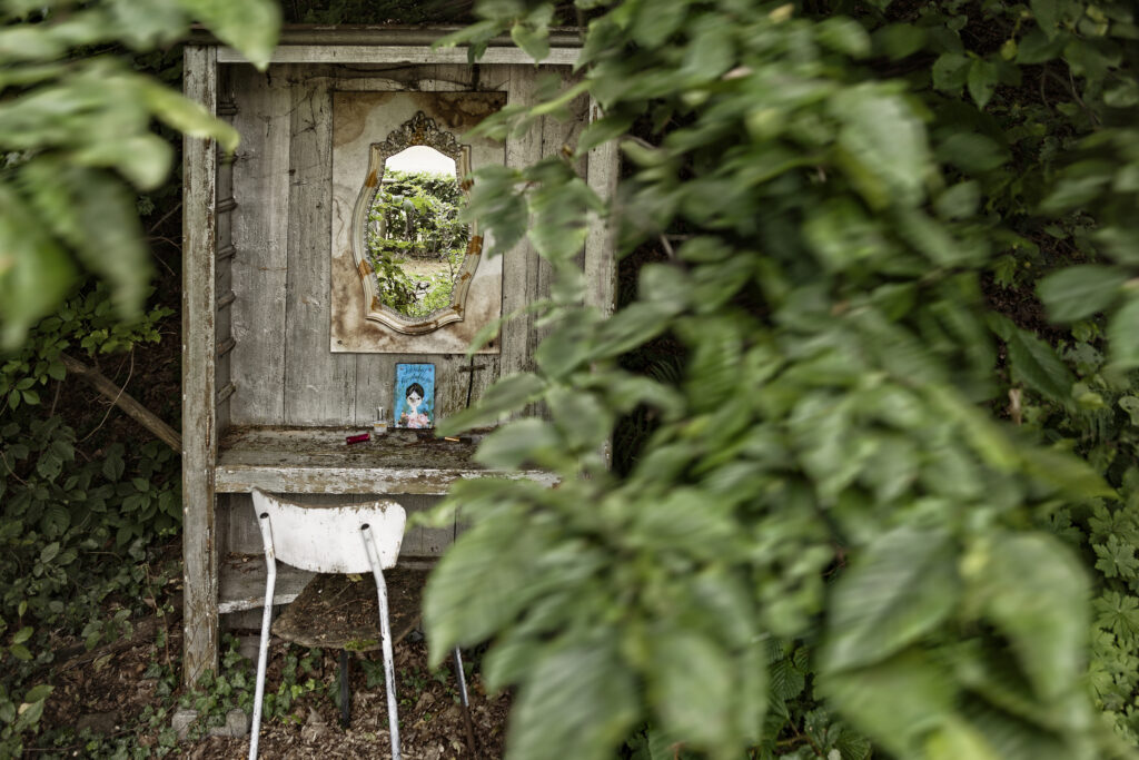 Alte hölzerne Nische mit Spiegel, Stuhl und Bild, verborgen im Garten des Möbel-Bahnhofs Bielefeld