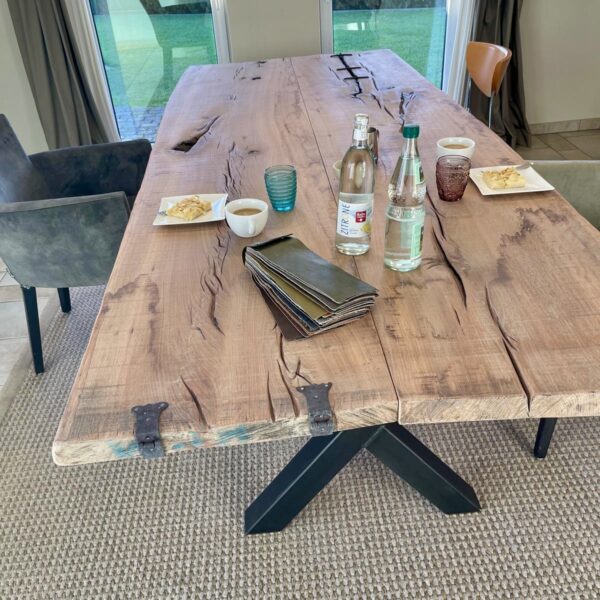 Massivholztisch mit Stahlbeinen in X-Form im Wohnraum eines Kunden, massive Holzplatte mit sichtbaren Rissen und Beschlägen